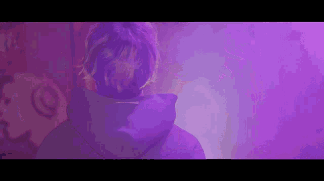 a man wearing a purple hoodie is standing in front of a purple background .