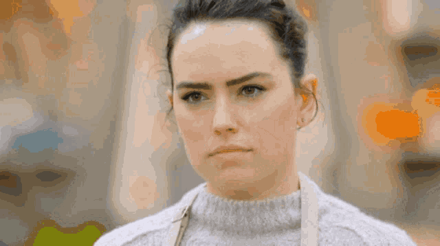 a woman wearing a grey sweater and apron looks serious