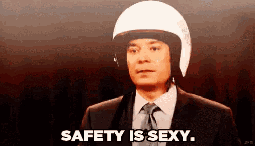 a man in a suit and tie is wearing a motorcycle helmet and says safety is sexy .