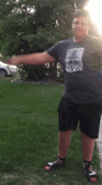 a man in a gray shirt and black shorts is standing in the grass with his hands in the air .