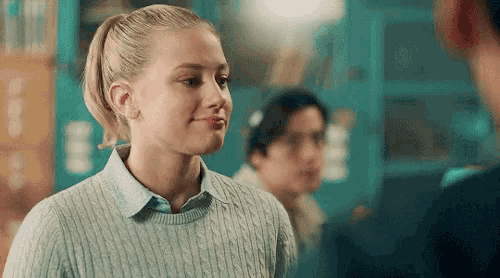 a woman in a sweater is smiling while standing next to a man in a room .