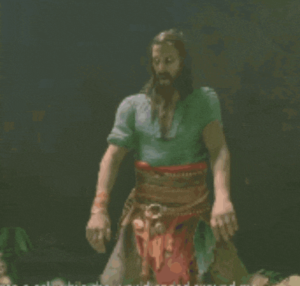 a man with long hair and a beard is standing in a dark room with his arms outstretched .