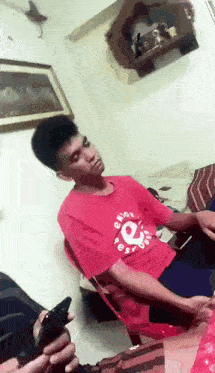 a man in a red shirt with the letter e on it sits in a chair