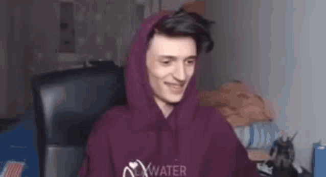 a man in a purple hoodie is sitting in a chair and smiling .