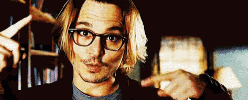 a man with long hair and glasses is pointing at something