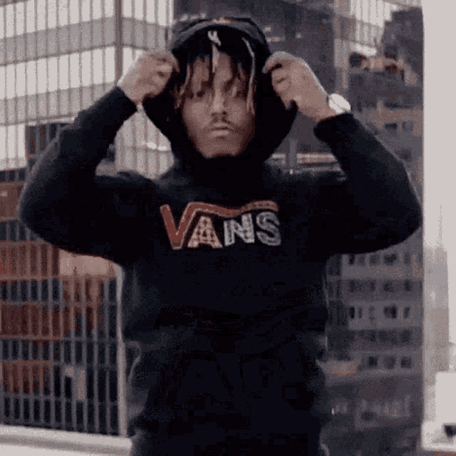 a man wearing a vans hoodie is standing in front of a tall building .