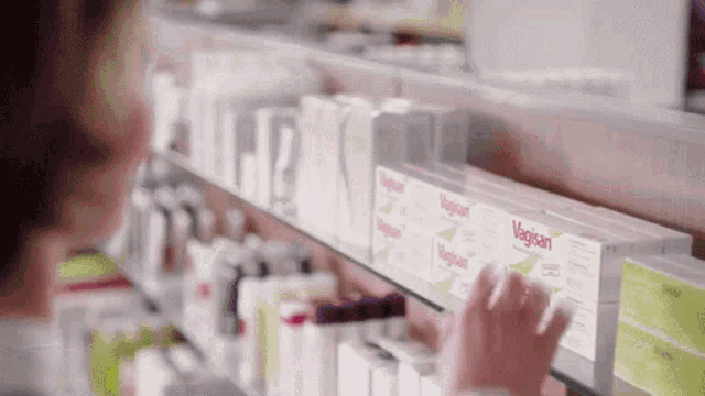 a woman is reaching for a box of vagisan in a pharmacy .
