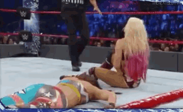 a woman is laying on the ground in a wrestling ring while a referee looks on .