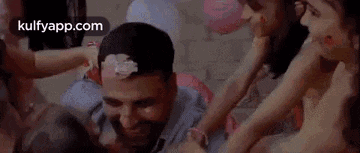a man with a cake on his head is surrounded by a group of children .