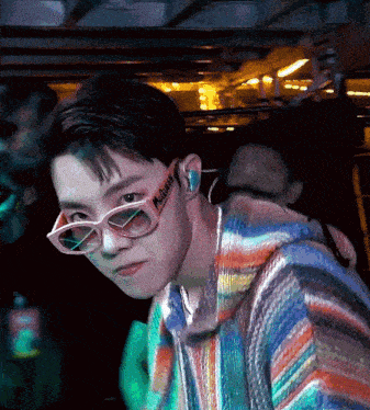 a young man wearing sunglasses and a colorful sweater has a sticker on his ear that says mr. queen