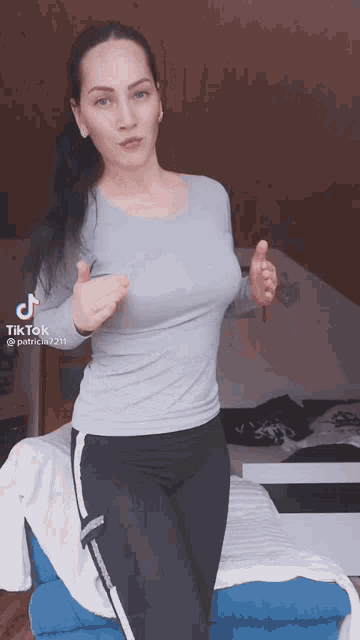 a woman in a grey shirt and black pants is giving a thumbs up sign