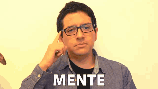 a man wearing glasses holds his finger to his forehead with the word mente written below him
