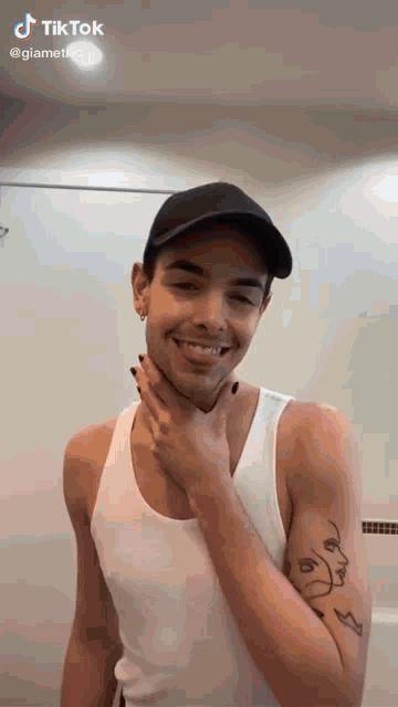 a man wearing a white tank top and a black hat is smiling .