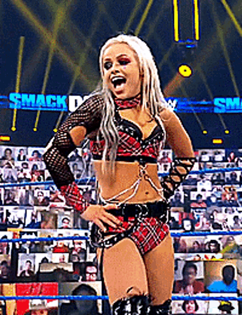 a woman in a plaid outfit is standing in a wrestling ring in front of a crowd .