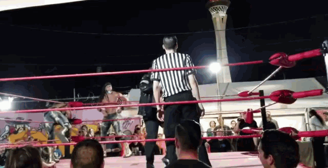 a referee in a striped shirt stands in a wrestling ring at night