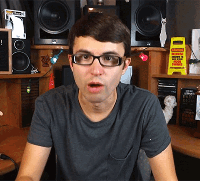 a man wearing glasses stands in front of a desk with a yellow sign that says caution beware wet floor towels