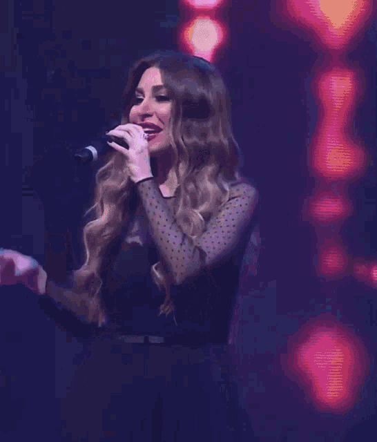 a woman in a black dress is singing into a microphone and making a peace sign