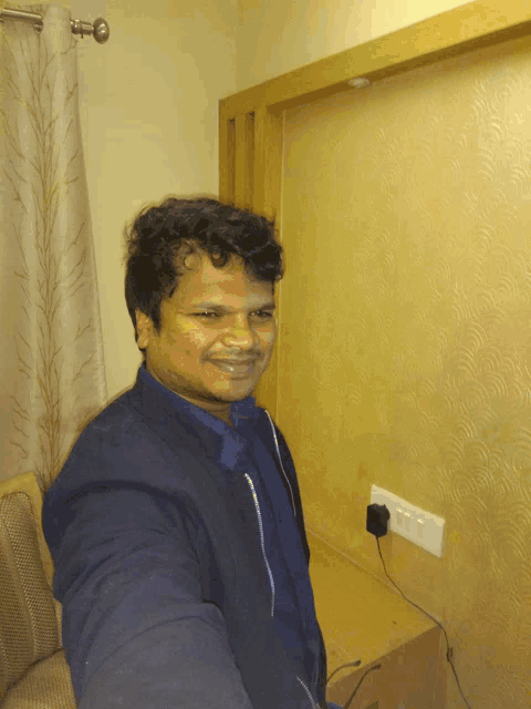 a man in a blue jacket is smiling in front of a wall