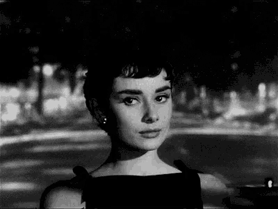 a black and white photo of a woman in a black dress standing in front of a street .