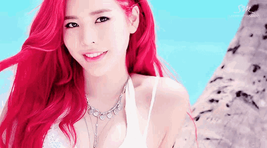 a woman with red hair is smiling and wearing a white tank top and necklace .