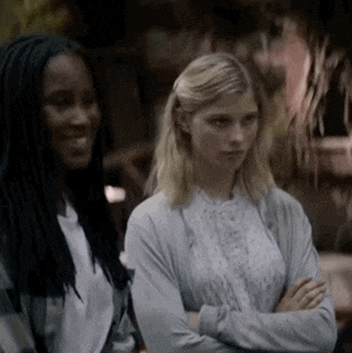two women are standing next to each other with their arms crossed and looking at each other .