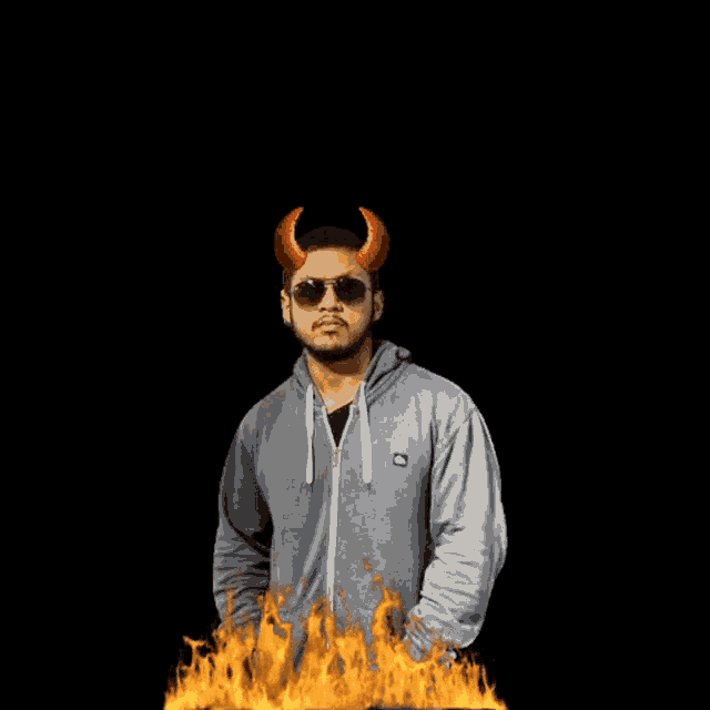 a man wearing devil horns stands in front of a fire