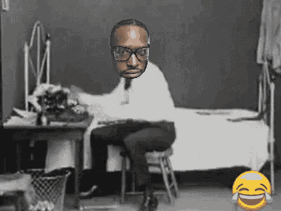 a black and white photo of a man wearing glasses sitting at a desk
