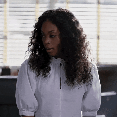 a woman with curly hair is wearing a white shirt and looking down .