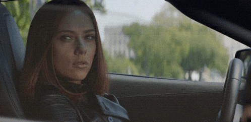 a woman in a black leather jacket is sitting in a car looking out the window