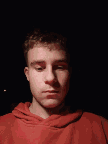 a young man wearing a red hoodie looks down at the camera