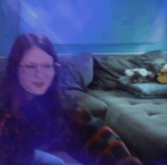 a woman wearing glasses is sitting on a couch smiling