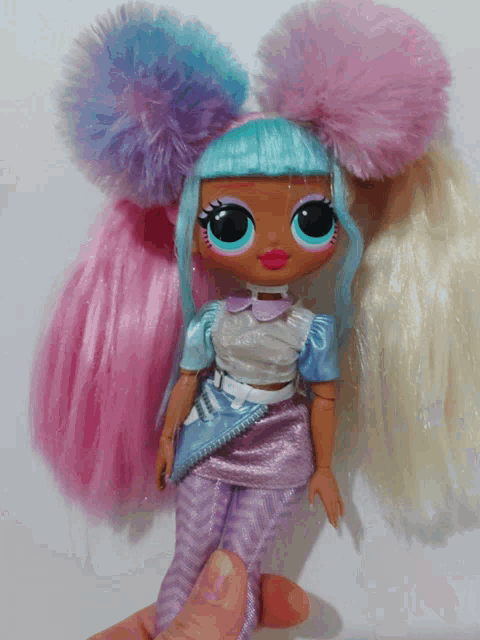 a doll with pink and blue hair is being held by a hand