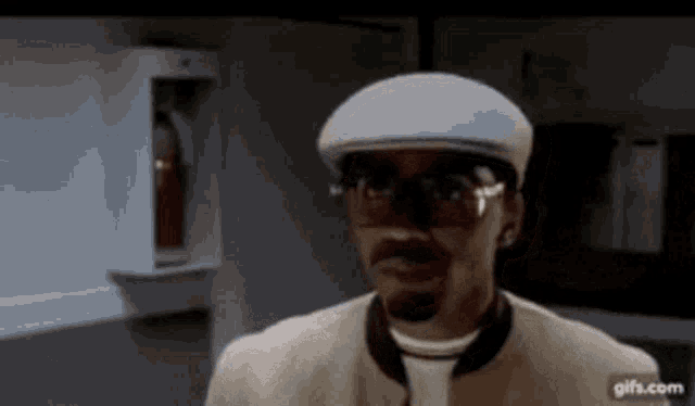 a man wearing a hat , sunglasses and a jacket is standing in a room .