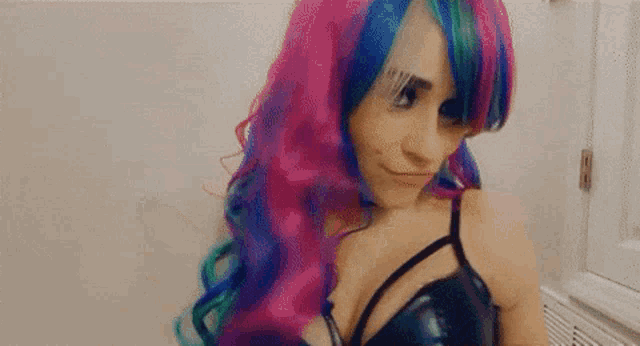a woman with rainbow hair and a black bra is standing in front of a white wall .