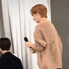 a man in a tan sweater is holding a microphone in his hand .