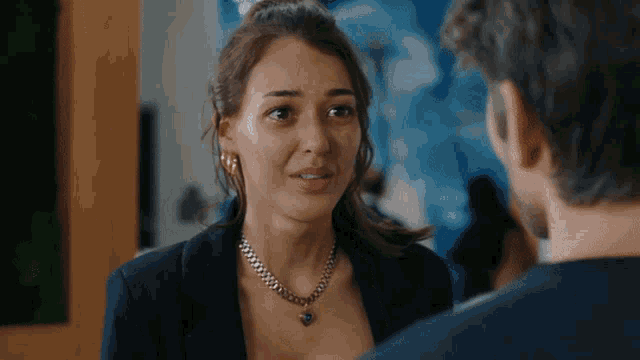 a woman wearing a necklace looks at a man