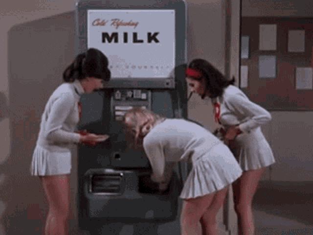 three girls are getting milk from a machine that says " cold refreshing milk "