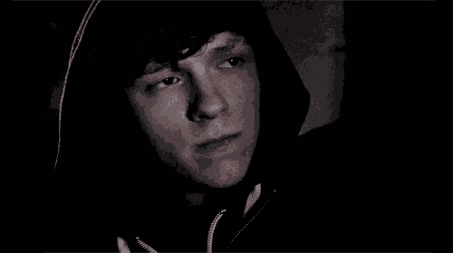 a young man in a black hoodie is looking at the camera .