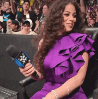 a woman in a purple dress is holding a microphone with a w logo on it .