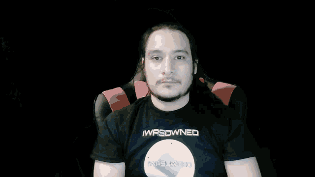 a man with long hair and a beard is sitting in a chair looking at the camera .