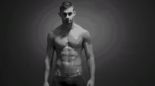 a shirtless man is standing in front of a black background with his arms outstretched in a black and white photo .
