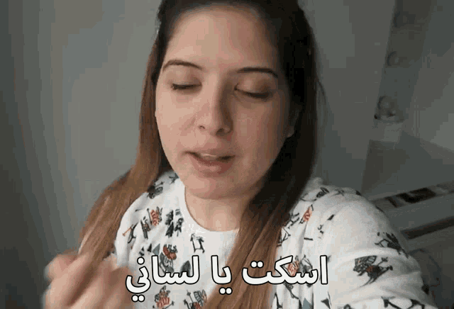 a woman with her eyes closed is wearing a white sweater with arabic writing on it