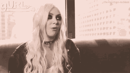 a woman with long blonde hair and a choker is sitting on a couch in a black and white photo .