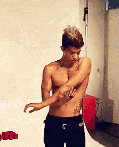 a shirtless man with a tattoo on his side is standing in front of a wall with the word lucky on it