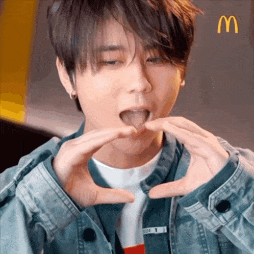 a young man is making a heart shape with his hands while eating a mcdonald 's hamburger