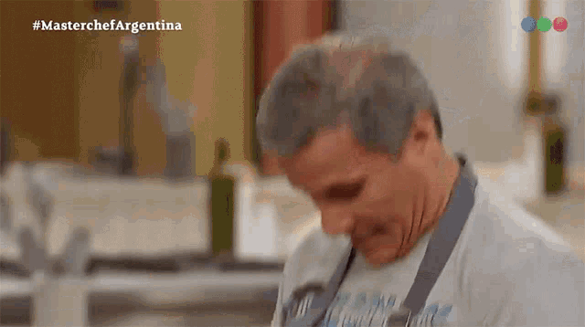 a man in a chef 's apron is standing in front of a television screen that says masterchef argentina on it