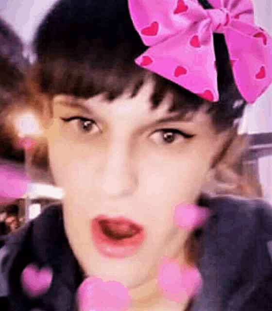 a woman wearing a pink bow with hearts on it is blowing hearts .