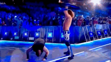 a wrestler is doing a handstand on the floor while another wrestler holds a rope .