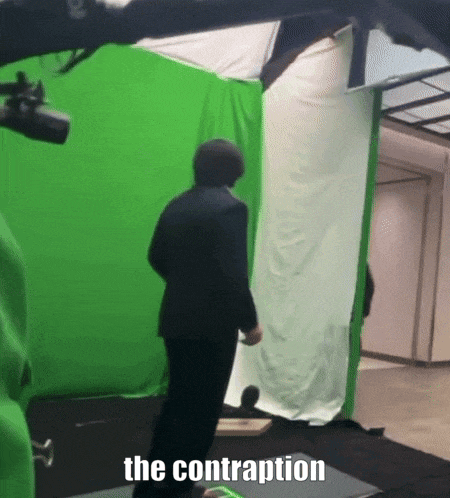 a man in a suit is standing in front of a green screen that says the contraption on it
