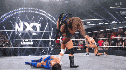 a female wrestler is being lifted by another wrestler in front of a nxt logo
